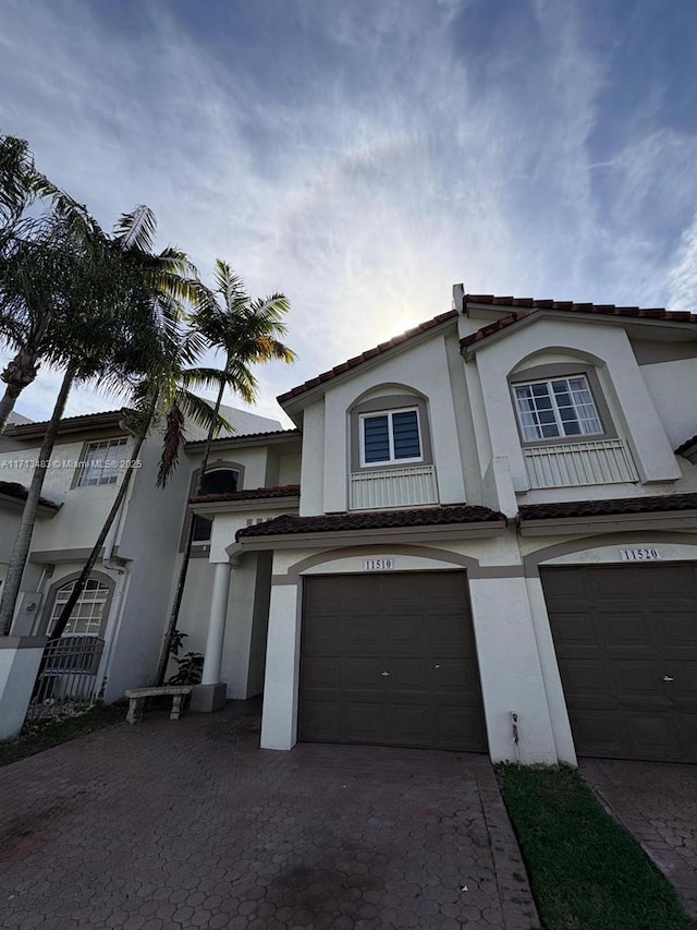 view of property featuring driveway, stucco siding, a tile roof, and an attached garage