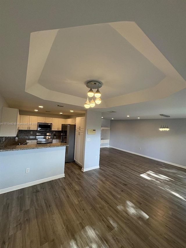 kitchen featuring appliances with stainless steel finishes, open floor plan, dark wood-style floors, and a tray ceiling