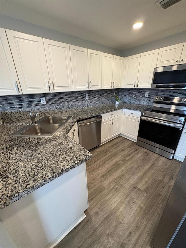 kitchen with white cabinetry, stainless steel appliances, backsplash, a sink, and dark wood-style floors