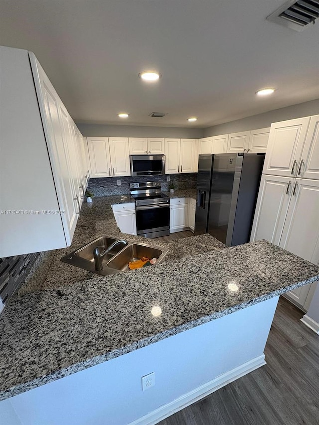 kitchen featuring visible vents, a peninsula, dark wood finished floors, appliances with stainless steel finishes, and a sink