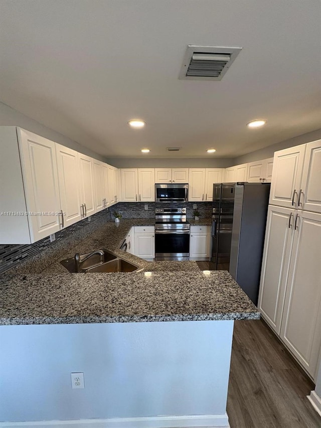 kitchen featuring white cabinets, dark stone countertops, kitchen peninsula, and appliances with stainless steel finishes