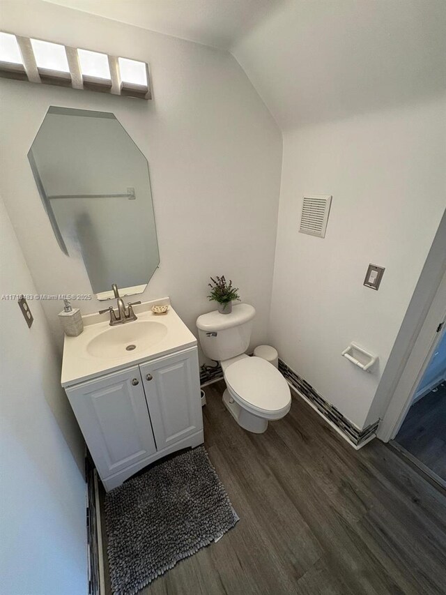 bathroom with vanity, wood-type flooring, lofted ceiling, and toilet