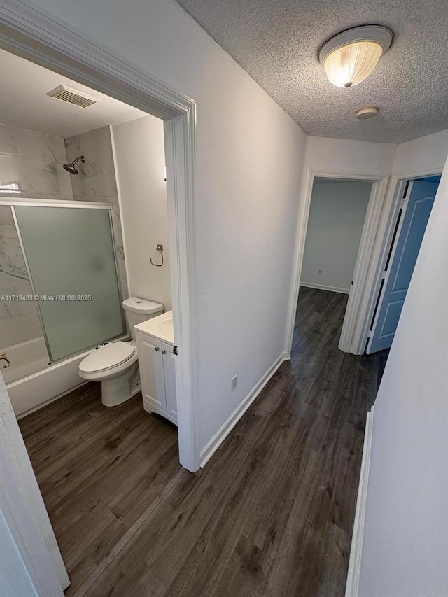 full bath featuring toilet, a textured ceiling, visible vents, combined bath / shower with glass door, and wood finished floors