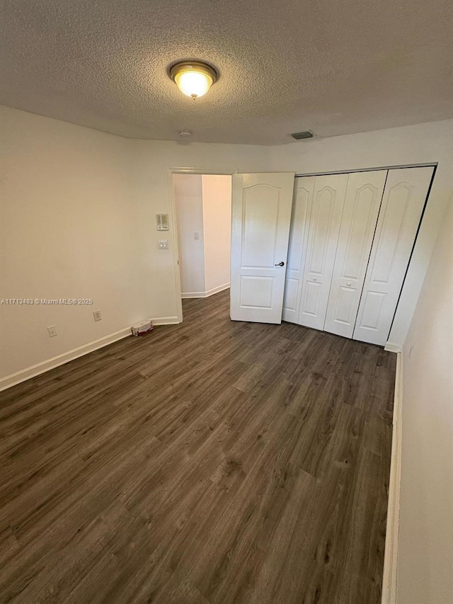 unfurnished bedroom featuring a closet, a textured ceiling, visible vents, baseboards, and dark wood-style floors