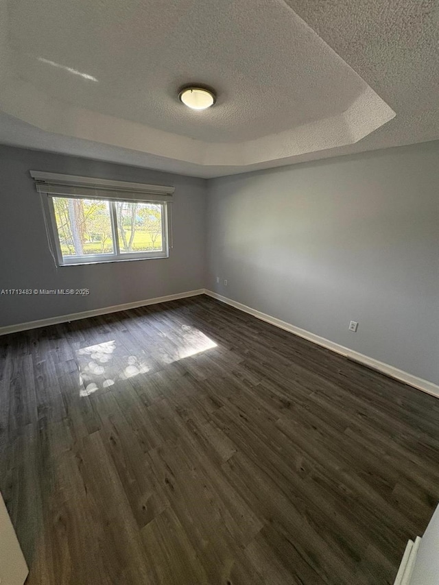 unfurnished room featuring a tray ceiling, dark wood-type flooring, and a textured ceiling