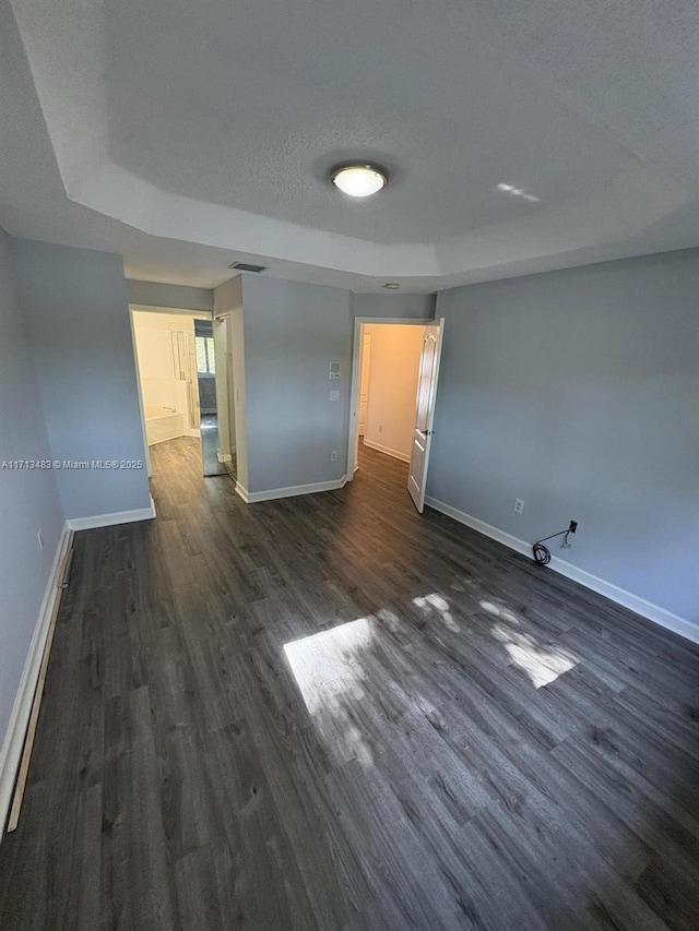 empty room featuring a raised ceiling, a textured ceiling, dark wood finished floors, baseboards, and visible vents