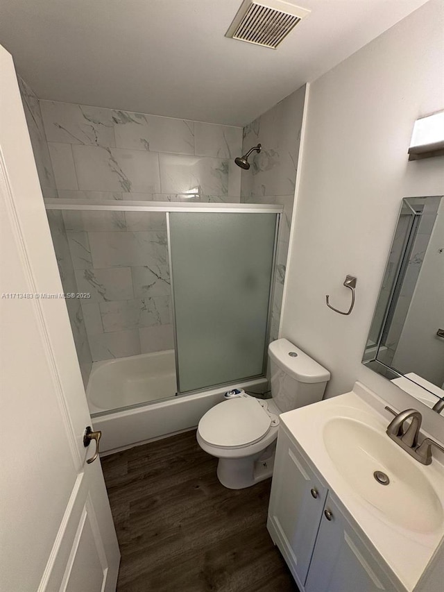 bathroom featuring toilet, vanity, wood finished floors, bath / shower combo with glass door, and visible vents