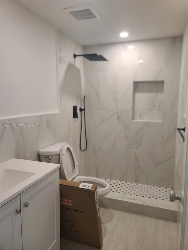 bathroom featuring a tile shower, vanity, tile walls, and toilet