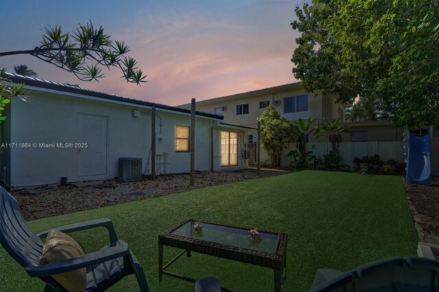 back house at dusk featuring cooling unit and a lawn