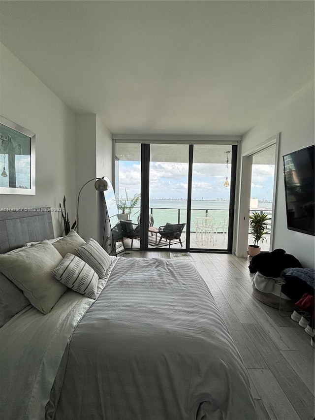 bedroom with access to exterior, wood-type flooring, multiple windows, and a wall of windows