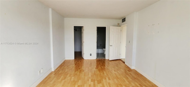 unfurnished bedroom featuring ensuite bathroom, wood-type flooring, and a walk in closet