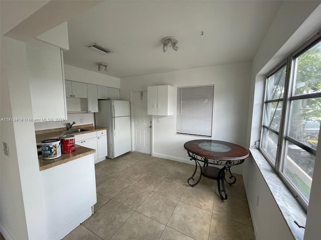 kitchen with white cabinets, white fridge, light tile patterned floors, and sink