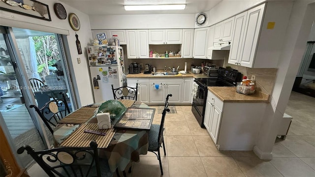 kitchen with light tile patterned flooring, sink, black / electric stove, white fridge, and white cabinetry