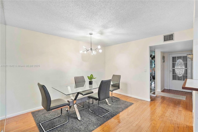 dining space featuring an inviting chandelier, wood finished floors, visible vents, and baseboards