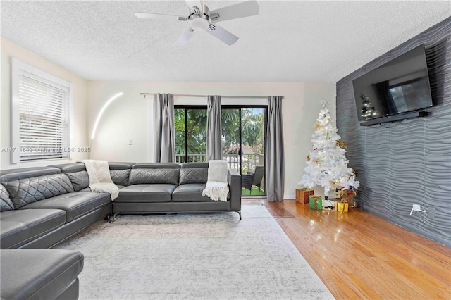 living room with a textured ceiling, an accent wall, a ceiling fan, and wood finished floors