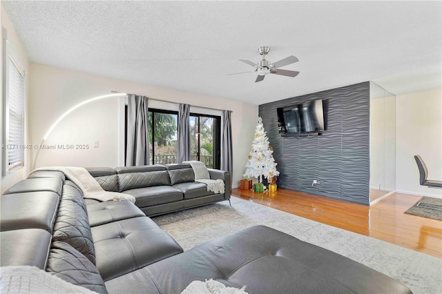 living room with a ceiling fan, a textured ceiling, wood finished floors, baseboards, and an accent wall