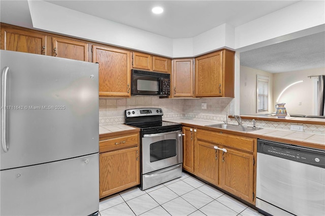 kitchen featuring decorative backsplash, tile countertops, appliances with stainless steel finishes, and a sink