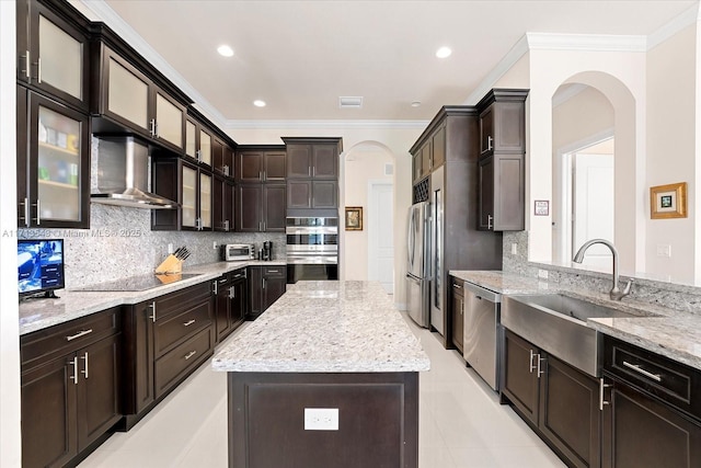 kitchen featuring appliances with stainless steel finishes, light stone countertops, wall chimney range hood, backsplash, and sink