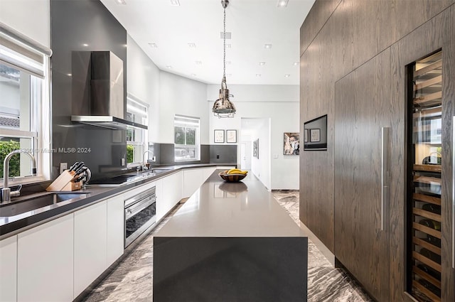 kitchen with a center island, stainless steel oven, sink, wall chimney range hood, and pendant lighting