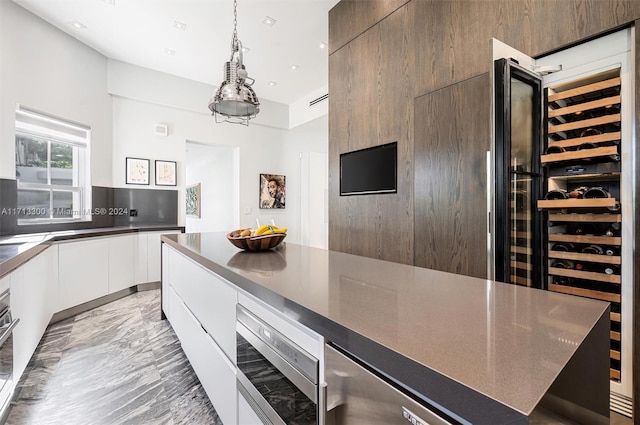 kitchen featuring white cabinets, oven, hanging light fixtures, and beverage cooler