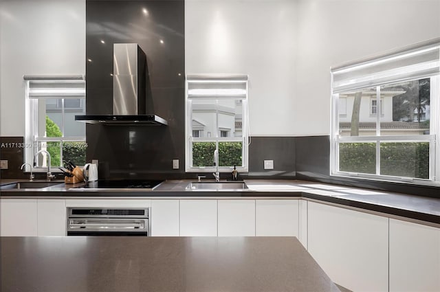 kitchen with wall chimney exhaust hood, stainless steel oven, white cabinets, and sink