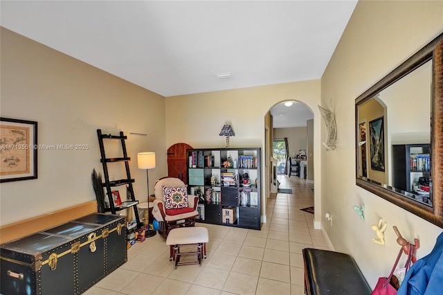 living area featuring arched walkways, light tile patterned flooring, and baseboards