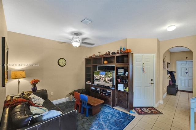 living room featuring arched walkways, light tile patterned floors, visible vents, a ceiling fan, and baseboards