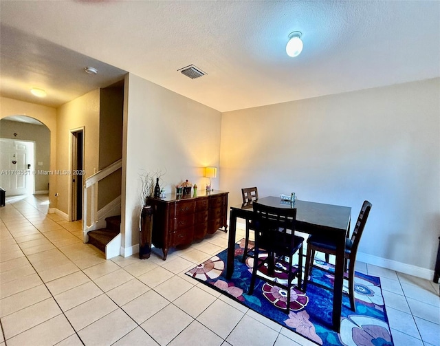 dining room with arched walkways, light tile patterned floors, visible vents, a textured ceiling, and stairs