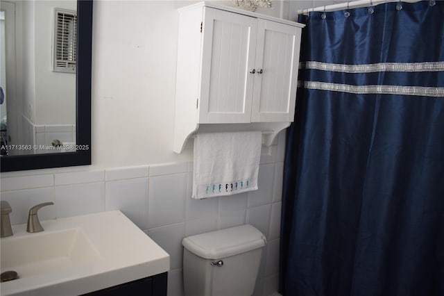 bathroom featuring walk in shower, vanity, toilet, and tile walls