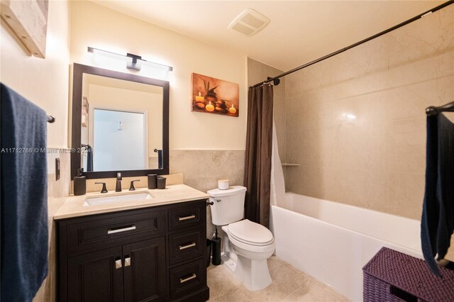 full bathroom featuring tile patterned floors, toilet, shower / bath combo with shower curtain, vanity, and tile walls