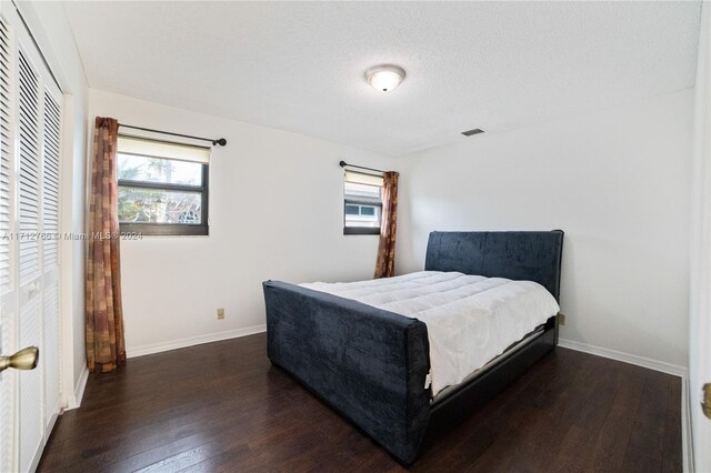 bedroom featuring a textured ceiling, dark hardwood / wood-style flooring, a closet, and multiple windows