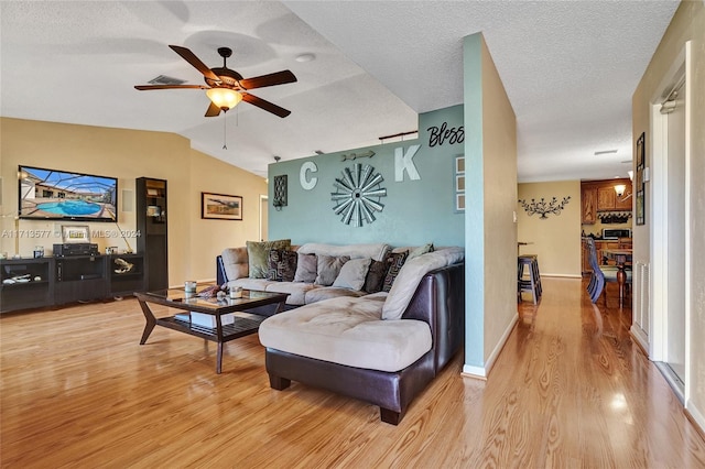 living room with ceiling fan, light wood-type flooring, a textured ceiling, and vaulted ceiling