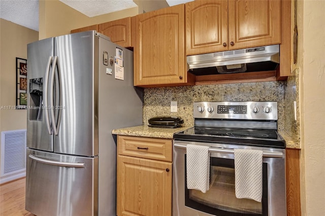 kitchen featuring light wood-type flooring, a textured ceiling, appliances with stainless steel finishes, tasteful backsplash, and light stone counters