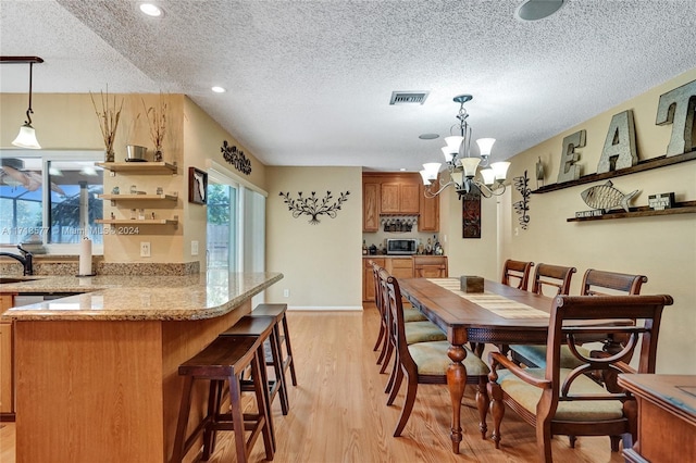 dining area featuring a notable chandelier, sink, a textured ceiling, and light hardwood / wood-style flooring