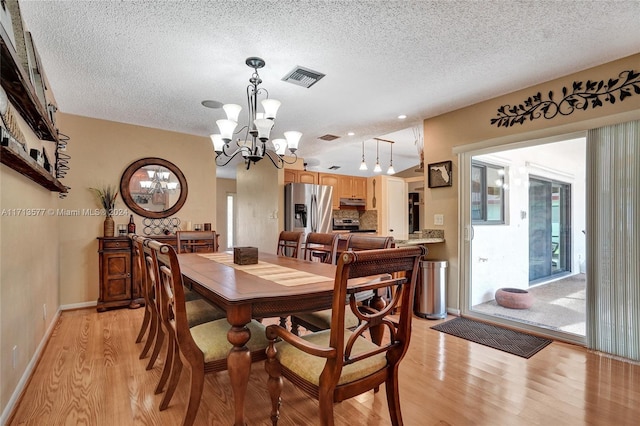 dining space featuring light hardwood / wood-style floors, a textured ceiling, and an inviting chandelier