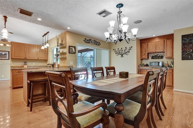 dining area featuring light hardwood / wood-style flooring, sink, a textured ceiling, and an inviting chandelier