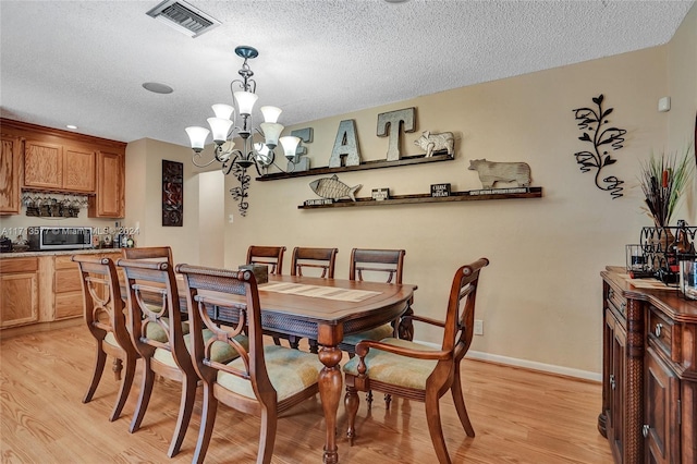 dining area with light hardwood / wood-style flooring, a chandelier, and a textured ceiling