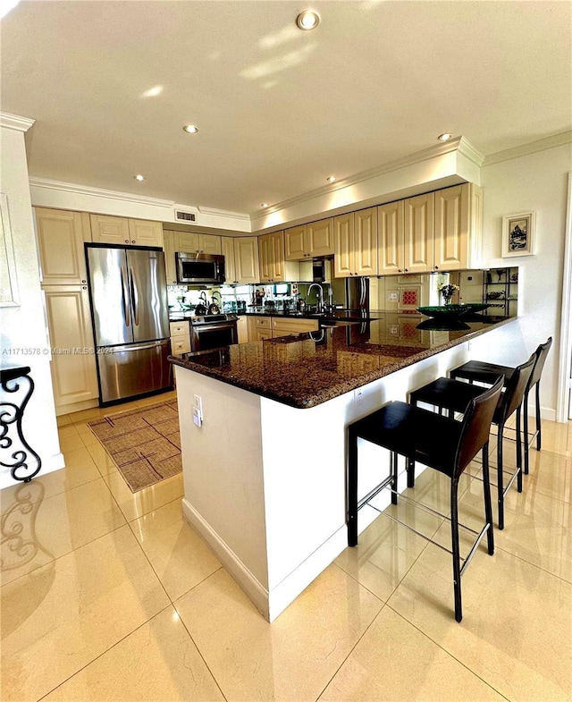 kitchen with kitchen peninsula, dark stone counters, stainless steel appliances, light tile patterned floors, and a breakfast bar area