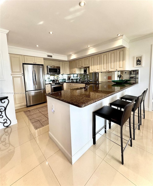 kitchen featuring kitchen peninsula, dark stone counters, a breakfast bar, light tile patterned flooring, and appliances with stainless steel finishes