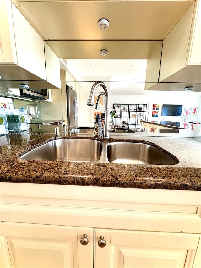 kitchen featuring ventilation hood, sink, dark stone countertops, white cabinets, and stainless steel refrigerator