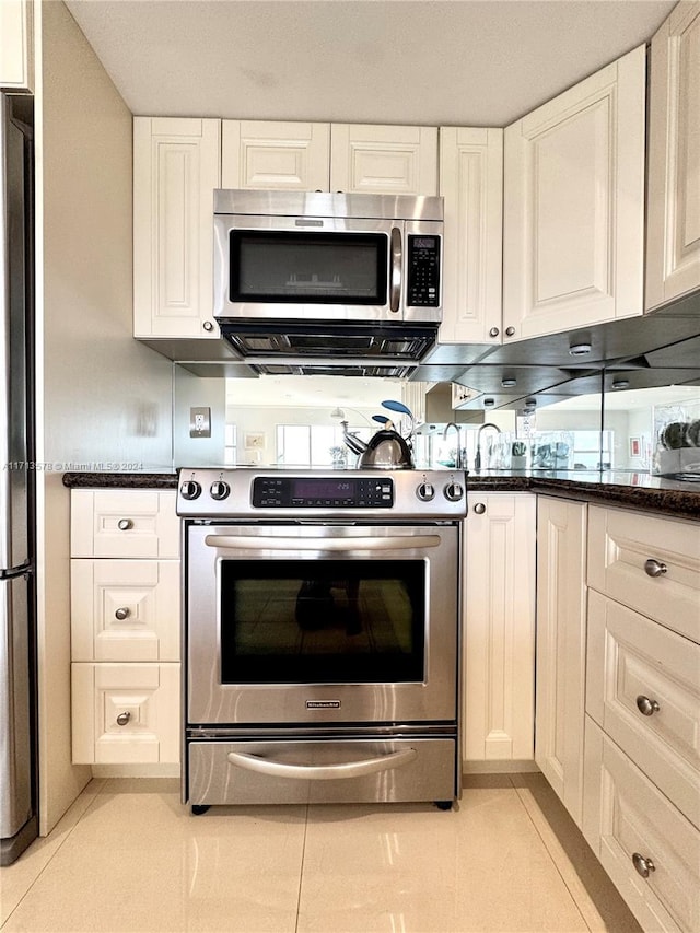 kitchen with light tile patterned floors, stainless steel appliances, white cabinetry, and dark stone countertops