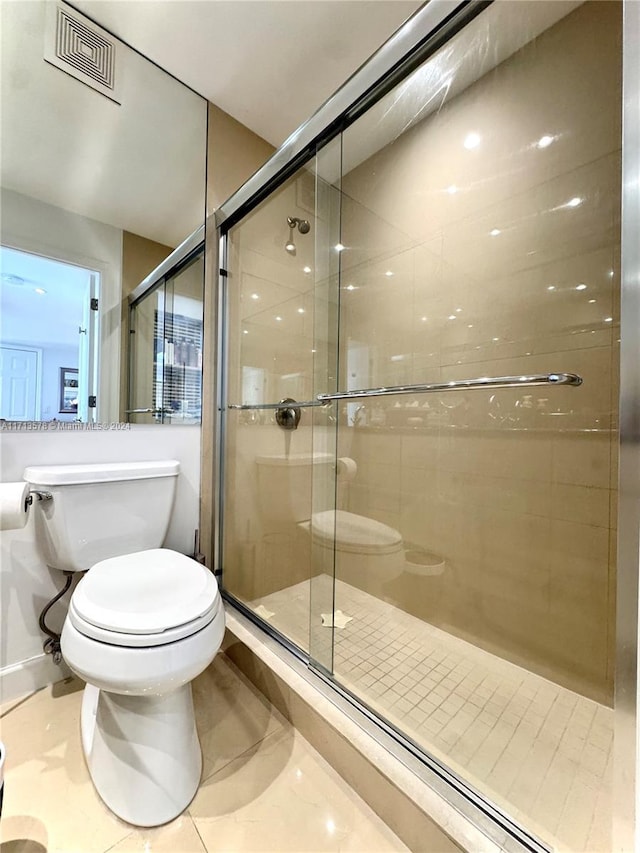 bathroom featuring a shower with door, tile patterned flooring, and toilet