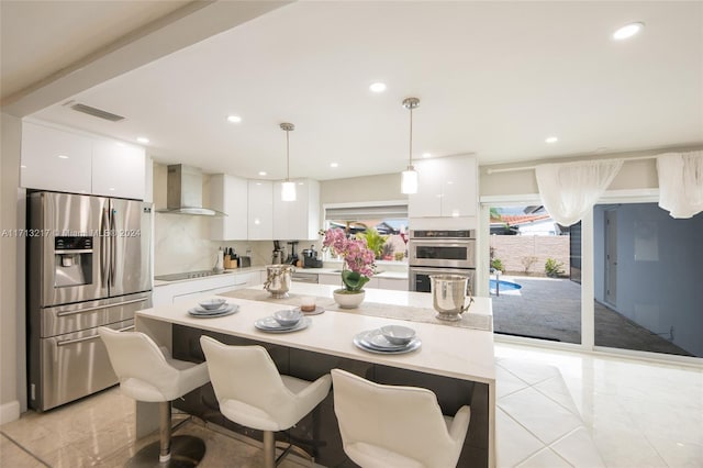 kitchen with white cabinets, appliances with stainless steel finishes, pendant lighting, and wall chimney exhaust hood