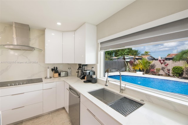 kitchen with black electric stovetop, stainless steel dishwasher, wall chimney range hood, light tile patterned floors, and white cabinets