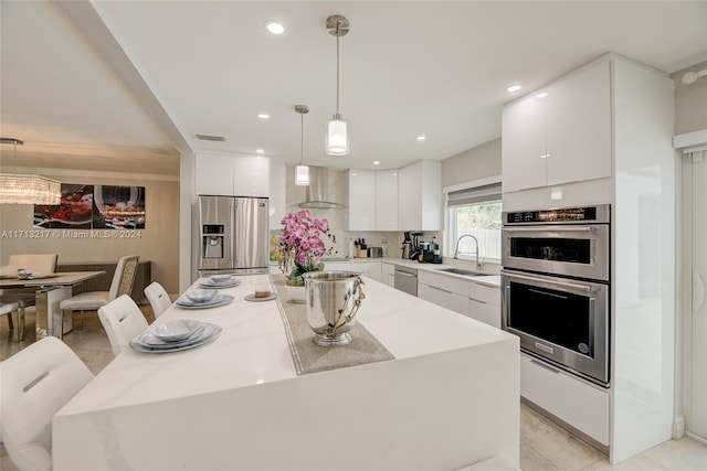 kitchen with stainless steel appliances, wall chimney range hood, decorative light fixtures, white cabinets, and a kitchen island