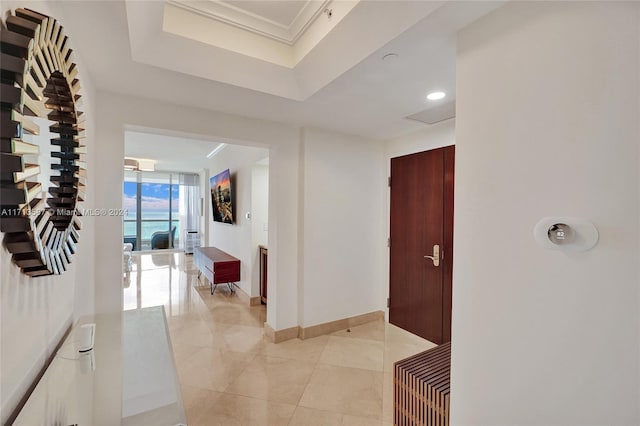 hall with crown molding, light tile patterned flooring, and a tray ceiling