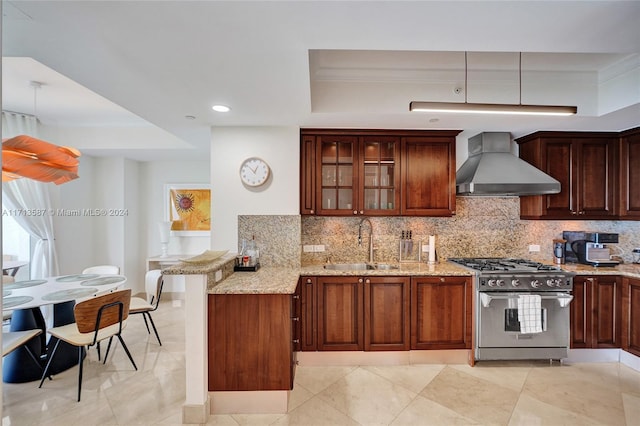 kitchen featuring high end stainless steel range oven, sink, wall chimney range hood, and a tray ceiling