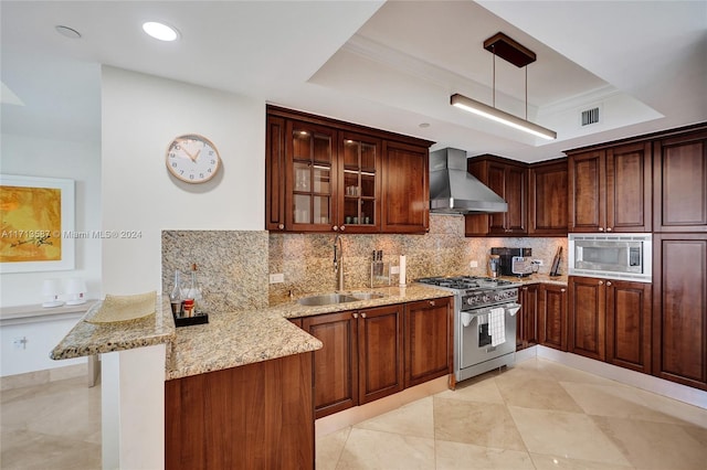 kitchen with kitchen peninsula, hanging light fixtures, a raised ceiling, appliances with stainless steel finishes, and wall chimney range hood