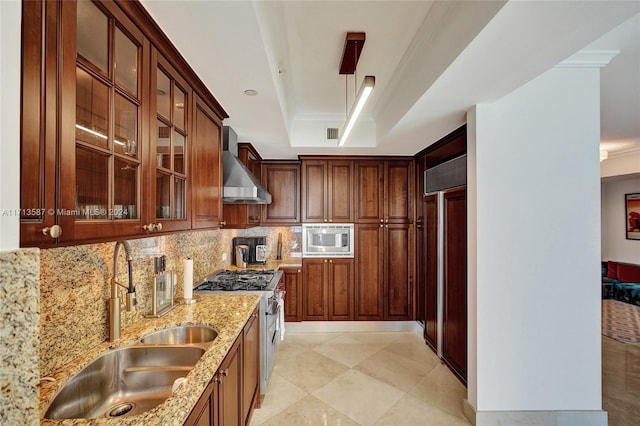 kitchen with light stone countertops, appliances with stainless steel finishes, wall chimney exhaust hood, sink, and a raised ceiling