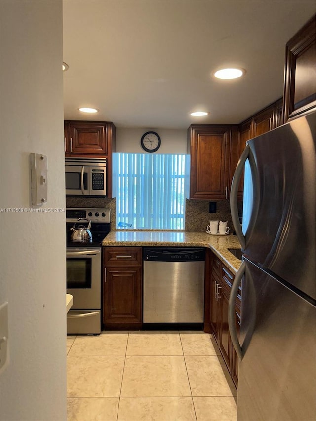 kitchen with decorative backsplash, light tile patterned floors, light stone countertops, and appliances with stainless steel finishes